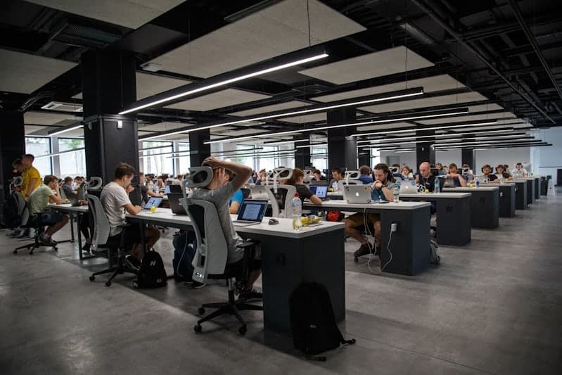 An open-plan floor of desks with colleagues working side by side at laptops.