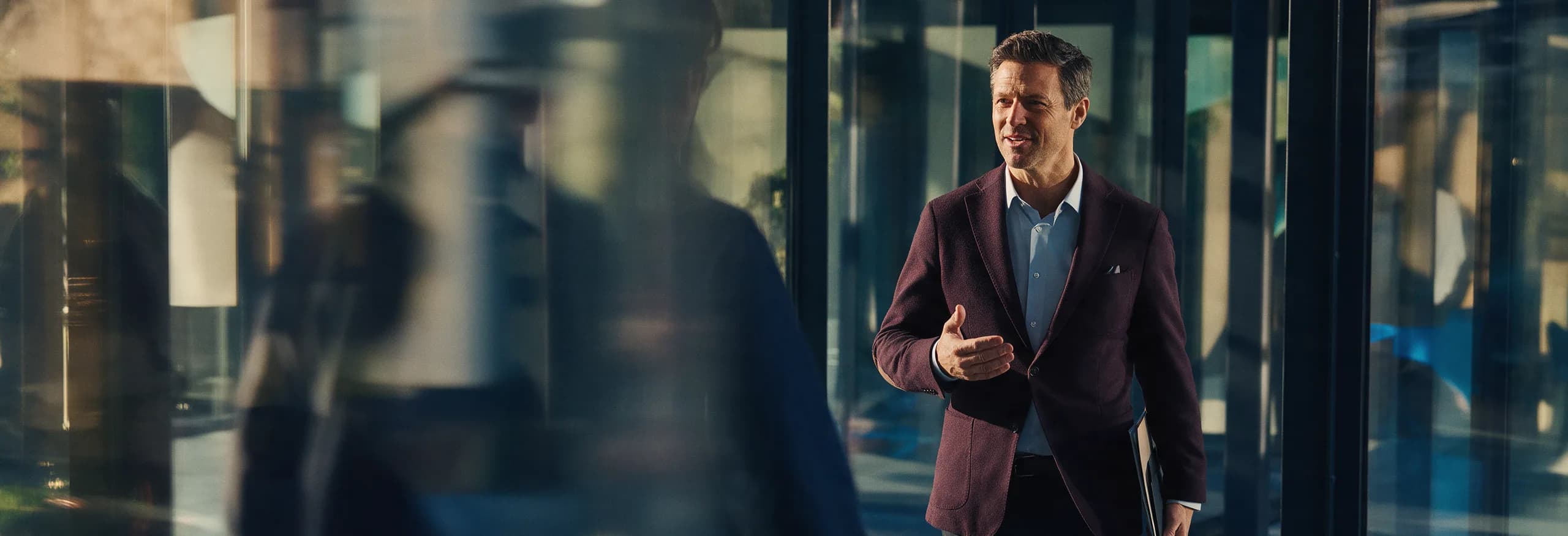 A colleague gesturing mid-conversation as he walks through a glass-fronted office