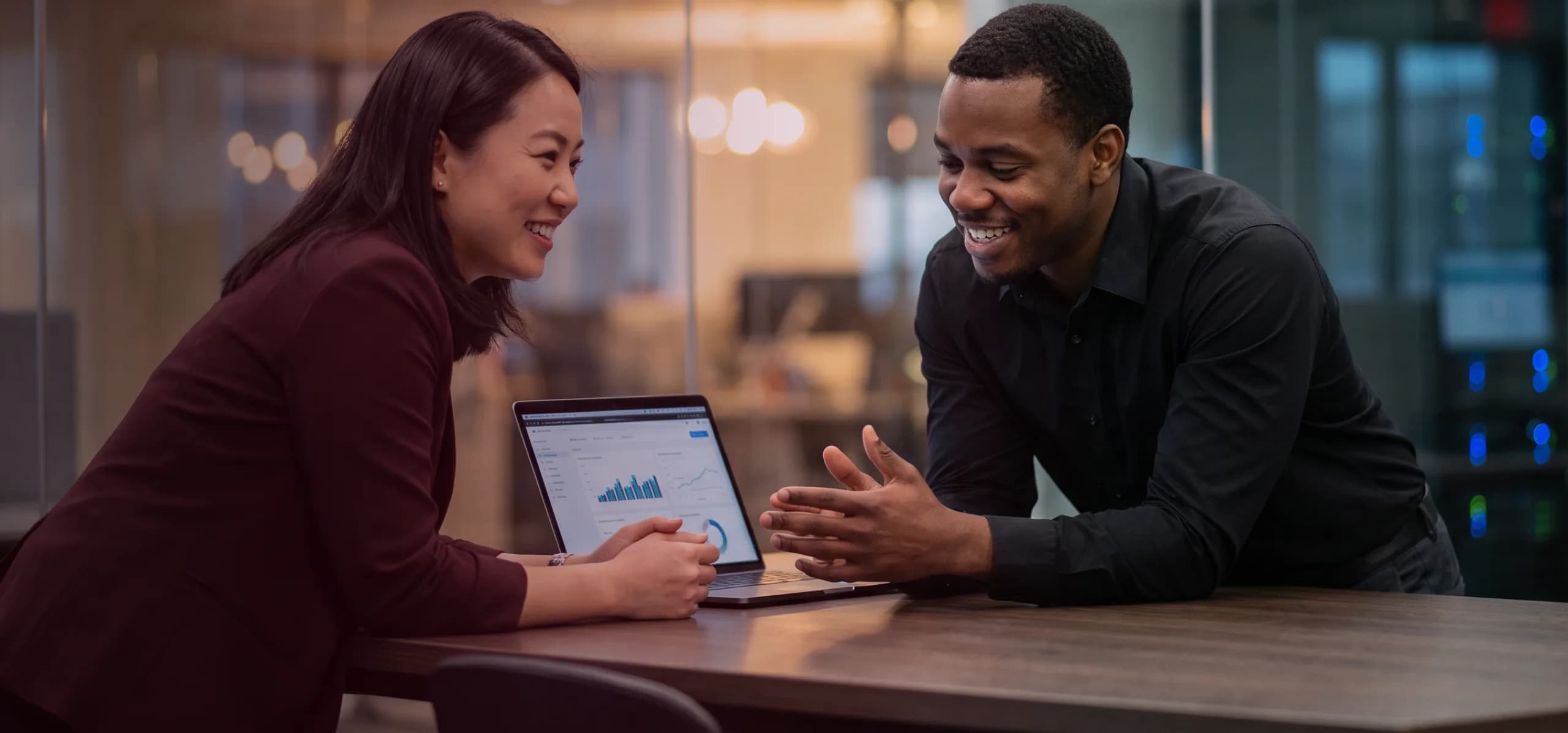 Two colleagues smiling over a laptop at a meeting table