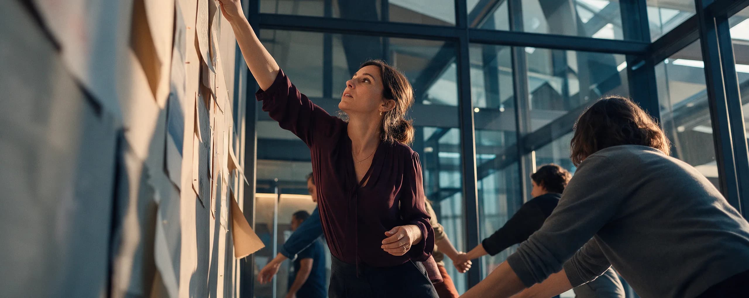 A woman pinning notes to a wall as colleagues work alongside her
