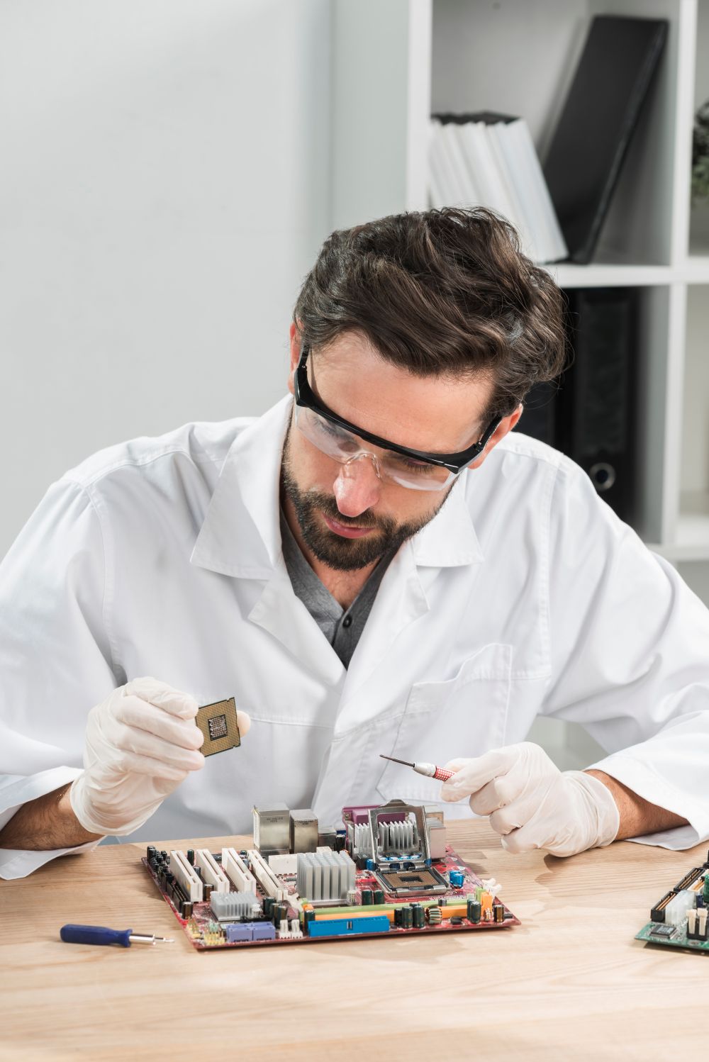 technician-holding-computer-chip-with-motherboard-wooden-desk