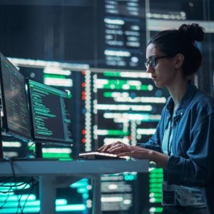 Person typing on computer with large screens in the background. All the screens are filled with code.